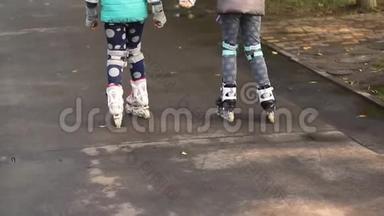 两个可爱的小白种人女孩在城市公园的雨后在潮湿的人行道上玩滑轮滑
